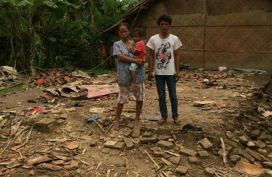 Samsudin (36) beserta istri dan anaknya berdiri di atas tanah bekas rumahnya yang ambruk tersapu angin kencang, Sabtu (20/01) siang.