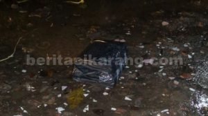 Bungkusan paket persegi empat yang dibungkus plastik warna hitam dan dilakban. Ditemukan oleh warga dan diduga berisi Bom.