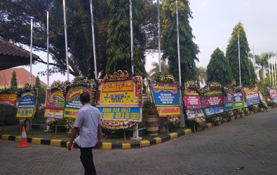 Salah seorang warga saat melintas diantara karangan bunga yang berjejer mengeliling pelataran gedung Bupati Bekasi, Rabu (12/06) sore.