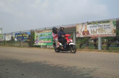 Salah seorang pengendara motor saat melintas diantara jejeran spanduk ucapan lebaran yang dipasang para Bakal Calon Kepala Desa di Jl. raya Inspeksi Kalimalang - Petigaan Kp. Patola Desa Pasir Tanjung Kecamatan Cikarang Pusat, Selasa (19/06).