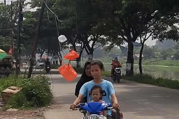 Salah seorang pengendara motor saat melintas jaringan kabel internet atau telepon menjuntai di Jalan Inspeksi Kalimalang, Desa Hegarmukti, Kecamatan Cikarang Pusat, Kamis (11/01).