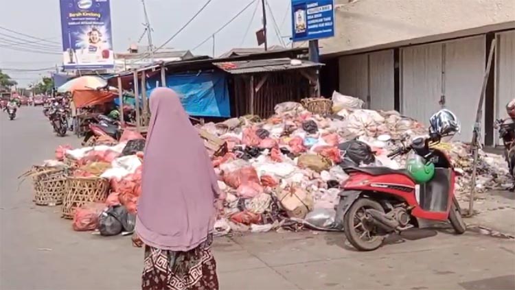 Salah seorang warga saat melintasi tumpukan sampah di tepi Jalan Yos Sudarso, Desa Cikarang Kota, Kecamatan Cikarang Utara, Rabu (17/04) siang.