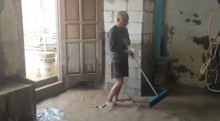 Salah seorang warga saat membersihkan rumahnya dari tumpukan lumpur imbas banjir luapan Kali Bekasi, Jum'at (19/04) sore.