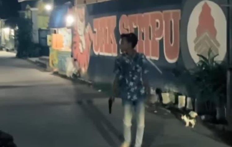 Dalam video berdurasi 54 detik yang tersebar luas, terlihat seorang pemuda mengenakan baju bermotif kembang dan celana jeans putih kedapatan membawa diduga senjata api jenis pitol.