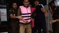 Mantan Sekdes Sumberjaya, SJ terlihat sumringah saat mengenakan rompi tahanan berwarna merah muda dan hendak dibawa ke Lembaga Pemasyarakatan Kelas IIA Cikarang. Ia bahkan tampak tersenyum lebar di hadapan kamera.