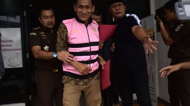 Mantan Sekdes Sumberjaya, SJ terlihat sumringah saat mengenakan rompi tahanan berwarna merah muda dan hendak dibawa ke Lembaga Pemasyarakatan Kelas IIA Cikarang. Ia bahkan tampak tersenyum lebar di hadapan kamera.