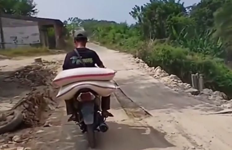 Salah seorang pengendara melintas di Jalan Raya CBL yang terletak di Kampung Sasak Bakar, Desa Kertamukti, Kecamatan Cibitung, Kabupaten Bekasi. Ruas jalan ini mengalami kerusakan parah sejak tahun lalu akibat tanah amblas. Agar memungkinkan dilalui kendaraan secara bersamaan dari dua arah, jalan tersebut ditutup sementara menggunakan plat besi.